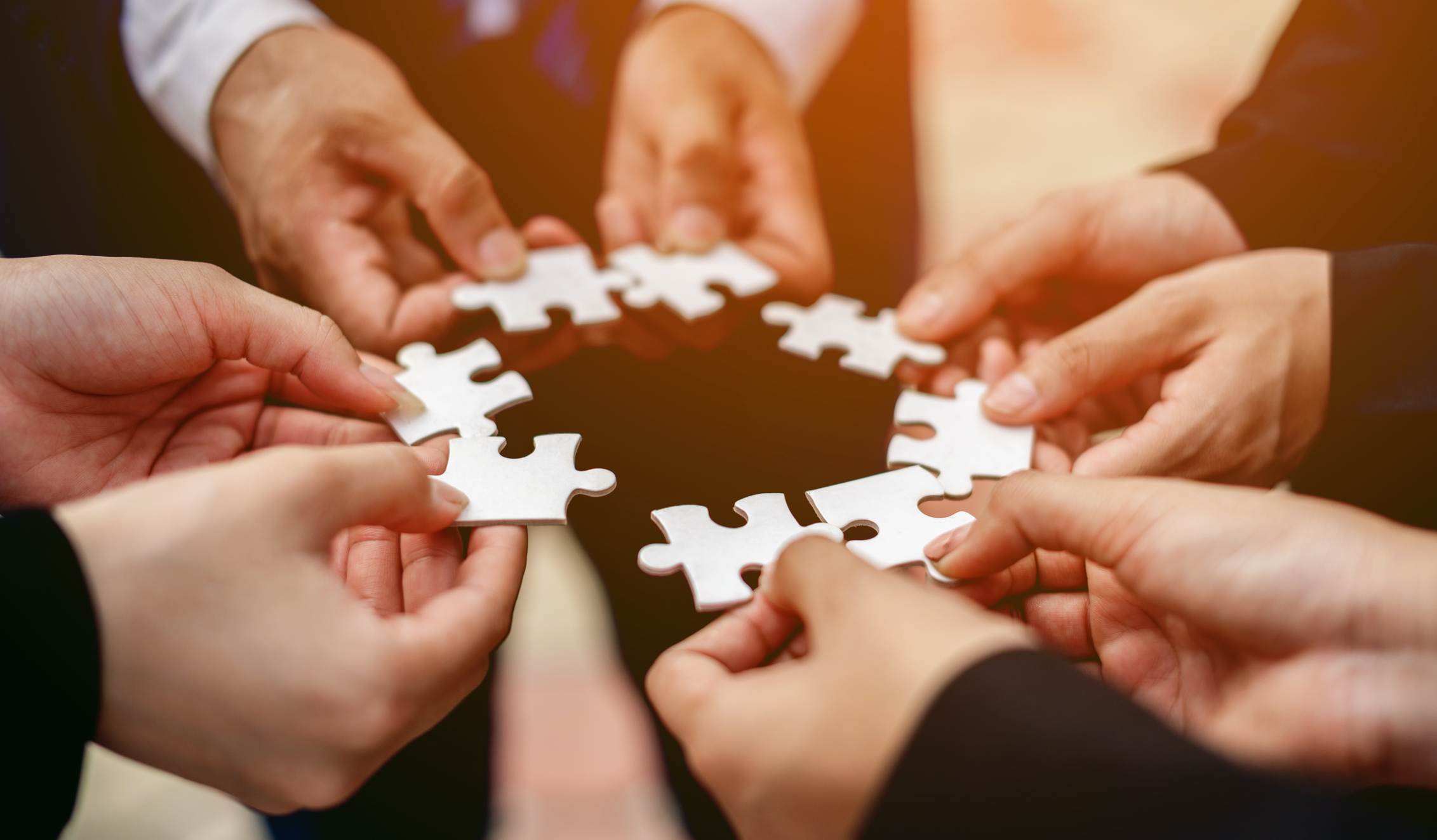 Photo of several hands connecting puzzle pieces.